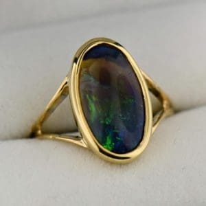 oval black crystal opal solitaire ring in yellow gold bezel with split shank